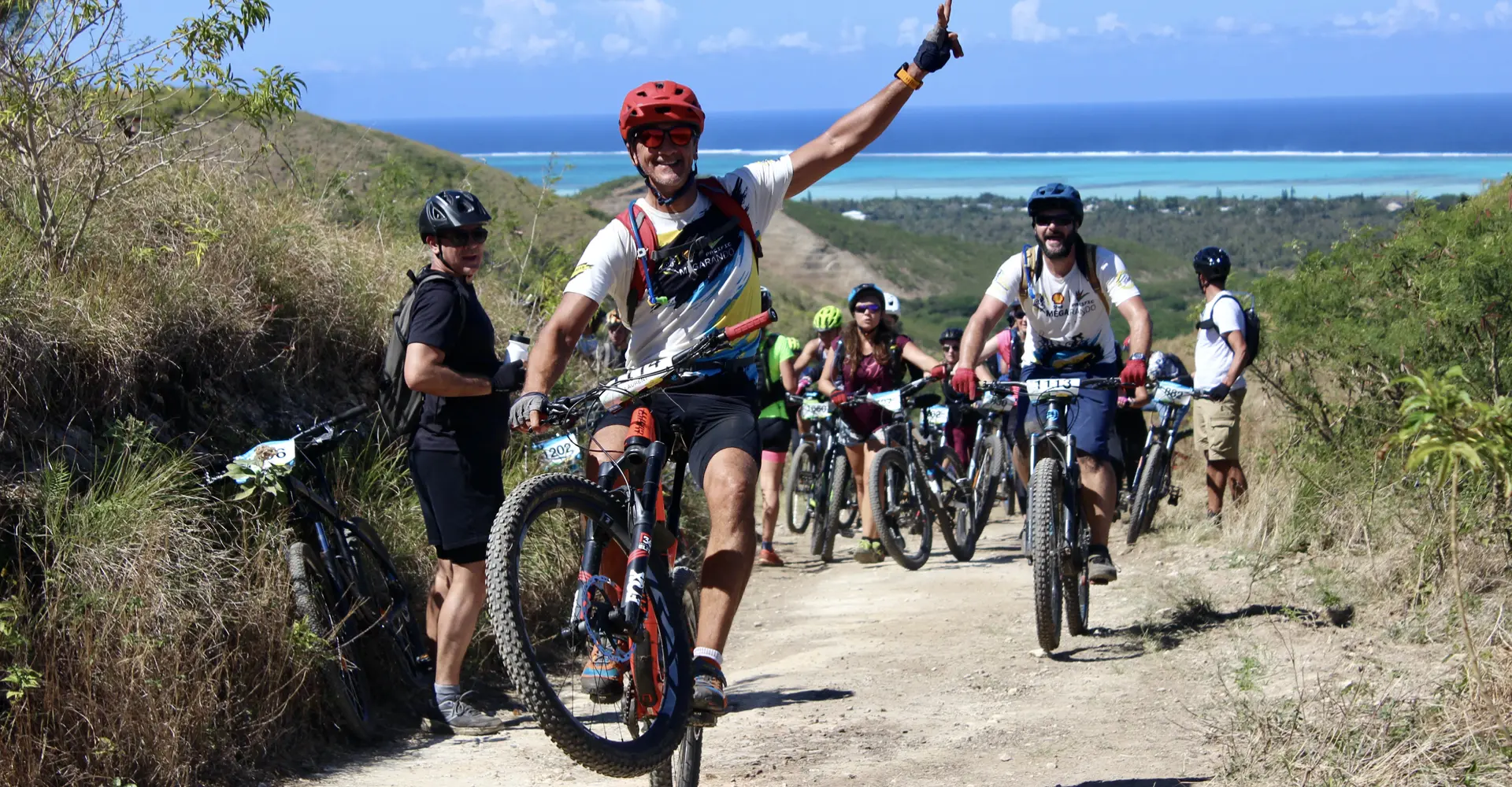 Ambiance Mégarando : cycliste bras levé devant le lagon de Nouvelle-Calédonie